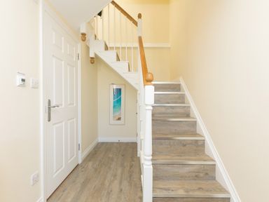 A hallway with wooden stairs and a closed white door at Cornerways in Carbis Bay
