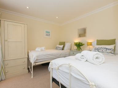 A bedroom with two single beds a wardrobe and a bedside table with flowers at Cornerways in Carbis Bay