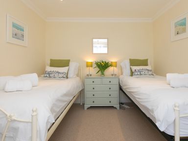 A bedroom with two single beds a chest of drawers with flowers and two lamps at Cornerways in Carbis Bay