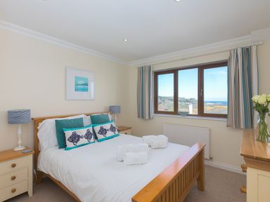 A bedroom with a wooden bed white bedding and blue cushions a window with striped curtains and two bedside tables at Cornerways in Carbis Bay