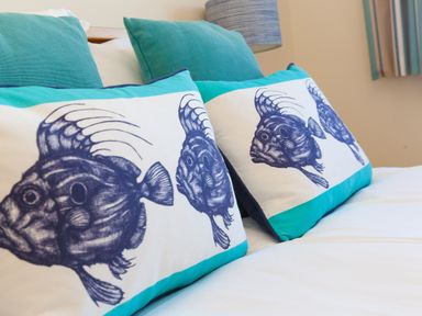 Two pillows with fish design and two turquoise cushions on a bed at Cornerways in Carbis Bay