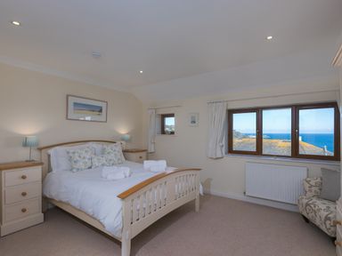 A bedroom with a double bed two bedside tables two lamps a window with sea view and an armchair at Cornerways Carbis Bay