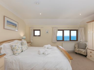 A bedroom with a large bed and rolled towels near windows with sea view and an armchair at Cornerways in Carbis Bay