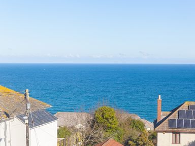 A view of the ocean with rooftops and trees in the foreground at Cornerways Carbis Bay