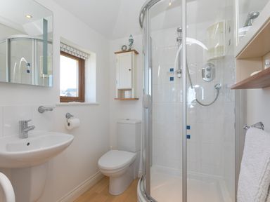 A bathroom with a shower enclosure toilet sink and wooden flooring at Cornerways in Carbis Bay