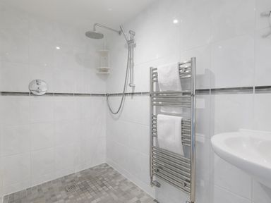 A tiled bathroom with a walk in shower a wall mounted towel rack with white towels and a white sink at Cornerways in Carbis Bay