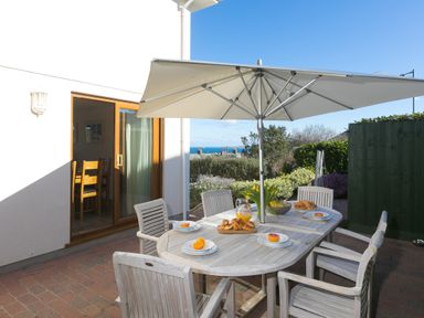 An outdoor patio with a wooden table and chairs under a large umbrella set with plates and croissants at Cornerways in Carbis Bay