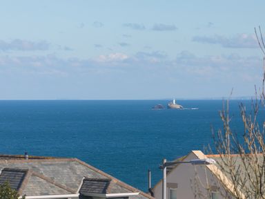 A view of the ocean with a lighthouse on a rock formation and rooftops in the foreground at Cornerways in Carbis Bay