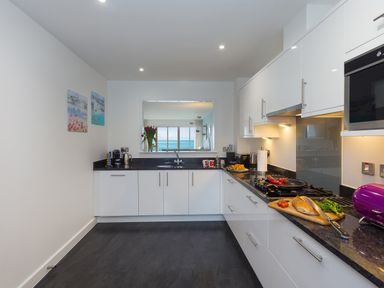 A kitchen with white cabinets black countertops and a window showing the sea at Elanora in Carbis Bay