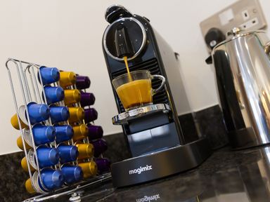 A black magimix coffee machine pouring coffee into a glass cup with colored coffee capsules on a rack beside it at Elanora in Carbis Bay