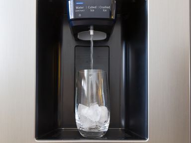 Water pouring into a glass with ice cubes from a refrigerator dispenser
