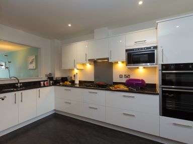 A kitchen with white cabinets black countertops and built in appliances at Elanora in Carbis Bay
