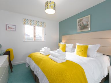 A bedroom with a double bed yellow throw and pillows white towels on bed a window and a painting on the wall at Elanora in Carbis Bay