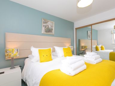 A bedroom with a bed with yellow pillows and blanket bedside tables and mirrored wardrobe doors at Elanora in Carbis Bay