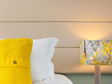 A bed with a yellow pillow and white sheets next to a lamp with a patterned shade at Elanora in Carbis Bay