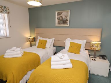 A bedroom with two single beds yellow blankets yellow pillows and bedside tables with lamps at Elanora in Carbis Bay