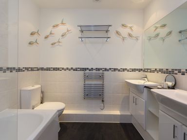 A bathroom with a bathtub toilet double sinks wall-mounted towel rack and fish decorations on the wall at Elanora in Carbis Bay