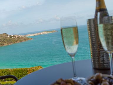 A table with two glasses of champagne and a bottle overlooking a coastal view with water and land at Elanora in Carbis Bay
