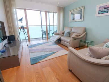A living room with beige sofas blue rug and a telescope by glass doors with an ocean view at Elanora in Carbis Bay
