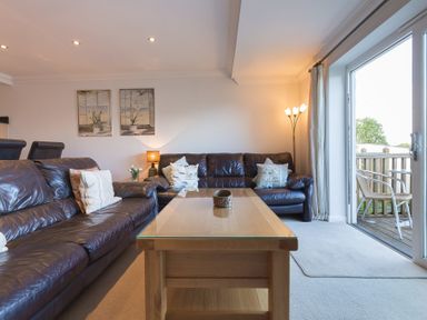 A living room with two brown leather couches a wooden coffee table and a floor lamp near a sliding glass door at Gennaker in Carbis Bay