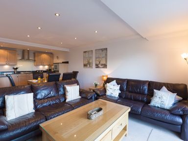 A living room with leather sofas and a wooden coffee table adjacent to a dining area and kitchen at Gennaker in Carbis Bay