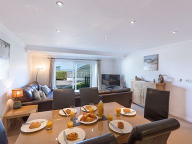 A dining table set with pastries and orange juice in a living room with leather sofas and a television at Gennaker in Carbis Bay