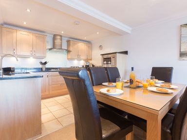 A kitchen and dining area with wooden cabinets and a table set with plates and glasses of orange juice at Gennaker in Carbis Bay