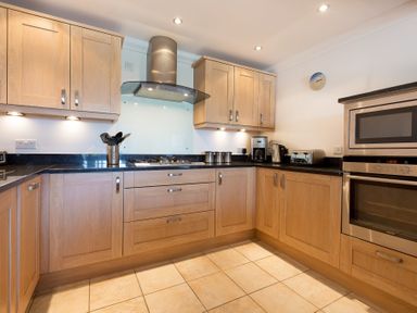 A kitchen with wooden cabinets black countertops a stainless steel oven and microwave and appliances on the countertop at Gennaker in Carbis Bay