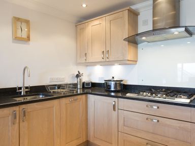 A kitchen with wooden cabinets black countertops a sink a stove a slow cooker and kitchen utensils at Gennaker in Carbis Bay