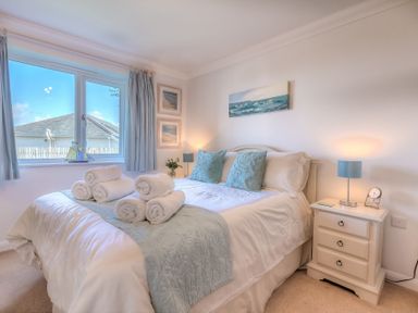 A bedroom with a bed with folded towels and blue pillows near a window and bedside tables at Gennaker in Carbis Bay