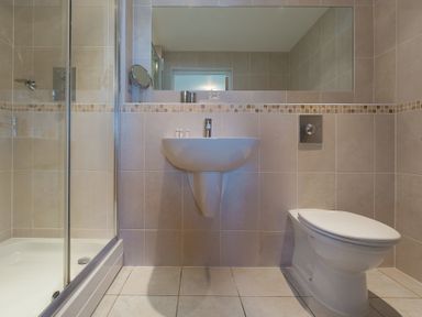 A bathroom with a shower, a wall-mounted sink, a toilet, and a large mirror at Gennaker in Carbis Bay