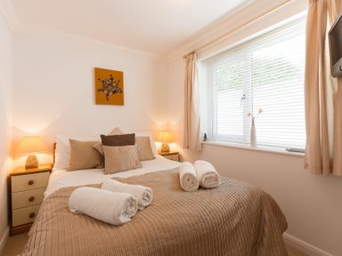 A bedroom with a bed made with brown striped bedding and rolled white towels on top with bedside tables and lamps on each side at Gennaker in Carbis Bay