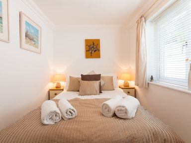 A bedroom with a double bed pillows and towels on the bed two bedside tables with lamps and a window with blinds at Gennaker Carbis Bay