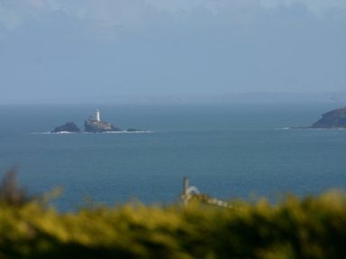 A lighthouse on a small rocky island in the sea with distant land on the horizon at Gennaker in Carbis Bay