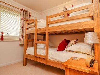 A bedroom with a wooden bunk bed and a wooden nightstand with a lamp and clock at Gennaker in Carbis Bay