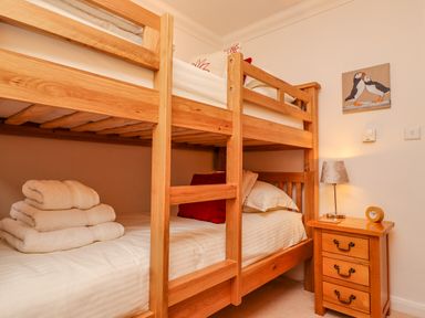 A bedroom with wooden bunk beds towels on lower bed a nightstand with a lamp and clock and a puffin painting on the wall at Gennaker in Carbis Bay