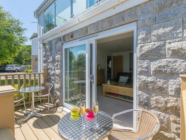 An outdoor balcony with metal tables and chairs and snacks next to a sliding door leading into a living room at Gennaker in Carbis Bay