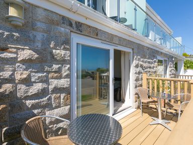 A balcony with two tables and four chairs outside a stone wall building with sliding glass doors at Gennaker in Carbis Bay