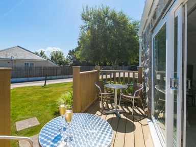 A small outdoor deck with two metal tables and three chairs overlooking a lawn at Gennaker in Carbis Bay