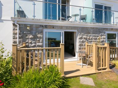 A patio with a wooden railing, metal chairs and tables outside a stone and white building at Gennaker in Carbis Bay
