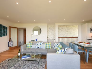 A living room with a gray sofa and patterned pillows next to a glass coffee table and dining table at Halcyon Cove in Carbis Bay