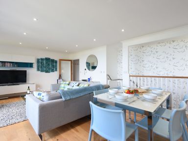 A living room and dining area with a grey sofa and blue chairs at Halcyon Cove in Carbis Bay