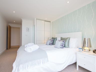A bedroom with a white bed and pillows next to a nightstand with a lamp at Halcyon Cove in Carbis Bay