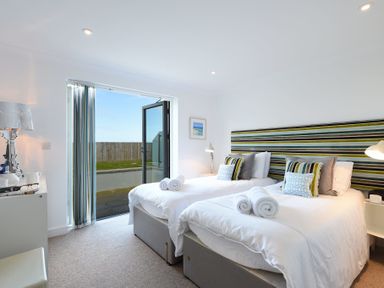 A bedroom with two single beds and open glass doors leading outside at Halcyon Cove in Carbis Bay