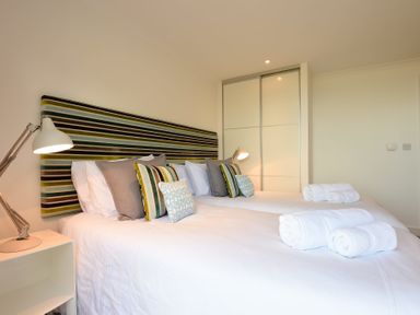A bedroom with two single beds with striped headboard and folded towels at Halcyon Cove in Carbis Bay