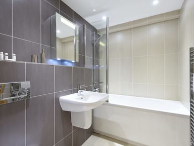 A bathroom with a wall-mounted sink bathtub shower and mirror at Halcyon Cove in Carbis Bay