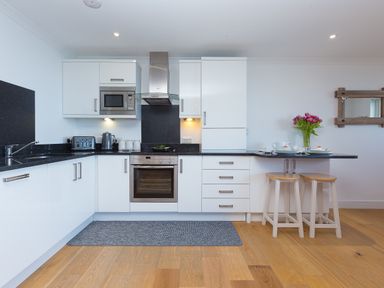 A kitchen with white cabinets black countertops and two stools at Kernows Dream in Carbis Bay
