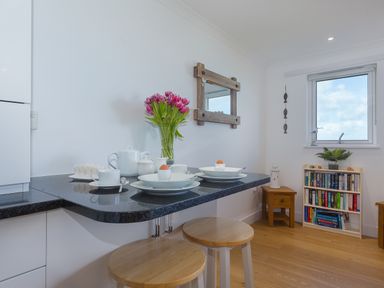 A kitchen counter with table settings and flowers next to a small bookcase and window at Kernow's Dream in Carbis Bay