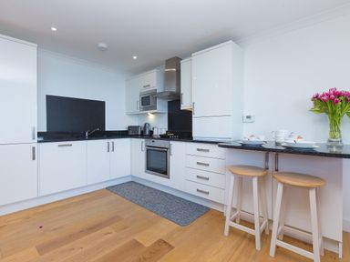 A modern kitchen with white cabinets black countertops wooden floor and two stools at Kernows Dream in Carbis Bay