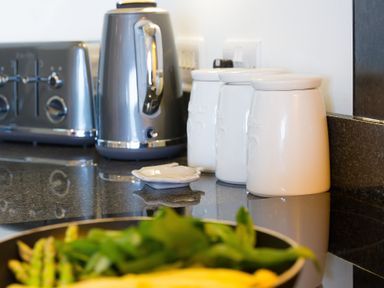 A kitchen counter with a silver toaster and kettle white canisters and a pan with green vegetables at Kernow's Dream in Carbis Bay